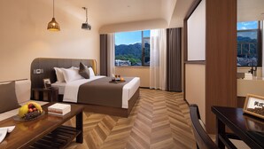A hotel room with a bed, bedside table, lamp, and a view of a cityscape. - Fenghuang Story Hotel (Xiangxi)