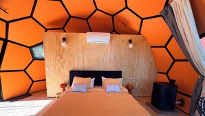A room with a hexagonal wall pattern, a wooden headboard, a bed with multiple pillows, a bedside table, and a small black speaker.