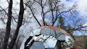 A hexagonal mirror sculpture surrounded by trees.