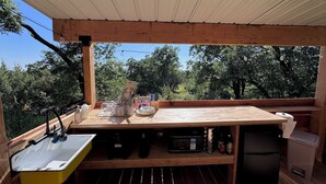 A wooden deck with a sink, a microwave, and a refrigerator, surrounded by trees.