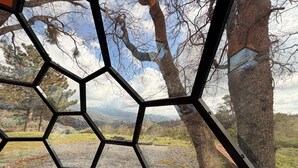 A hexagonal window frame with a view of a mountainous landscape, trees, and a clear sky.