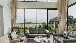 A spacious living area with a large window, a grey leather sofa, a smaller sofa, and a coffee table. - on the hill by the sea (Chandikanagar, Maharashtra)