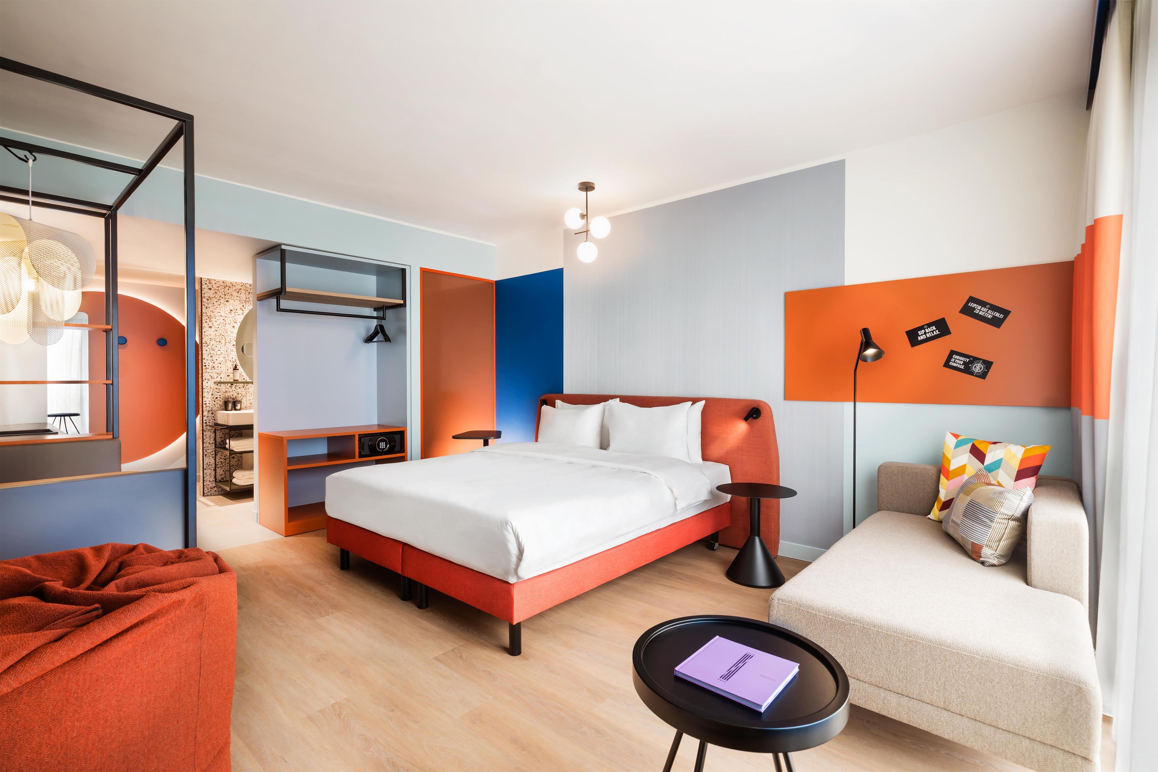 A modern hotel room with a bed, a sofa, a desk, and a wall with motivational quotes.
