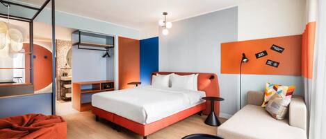 A modern hotel room with a bed, a sofa, a desk, and a wall with motivational quotes.