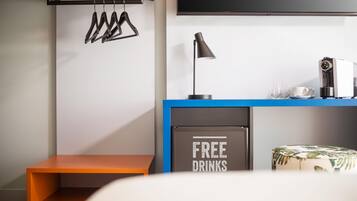 A modern room with a blue desk, a coffee machine, a sign offering free drinks, a hanging coat rack, and a television mounted on the wall.