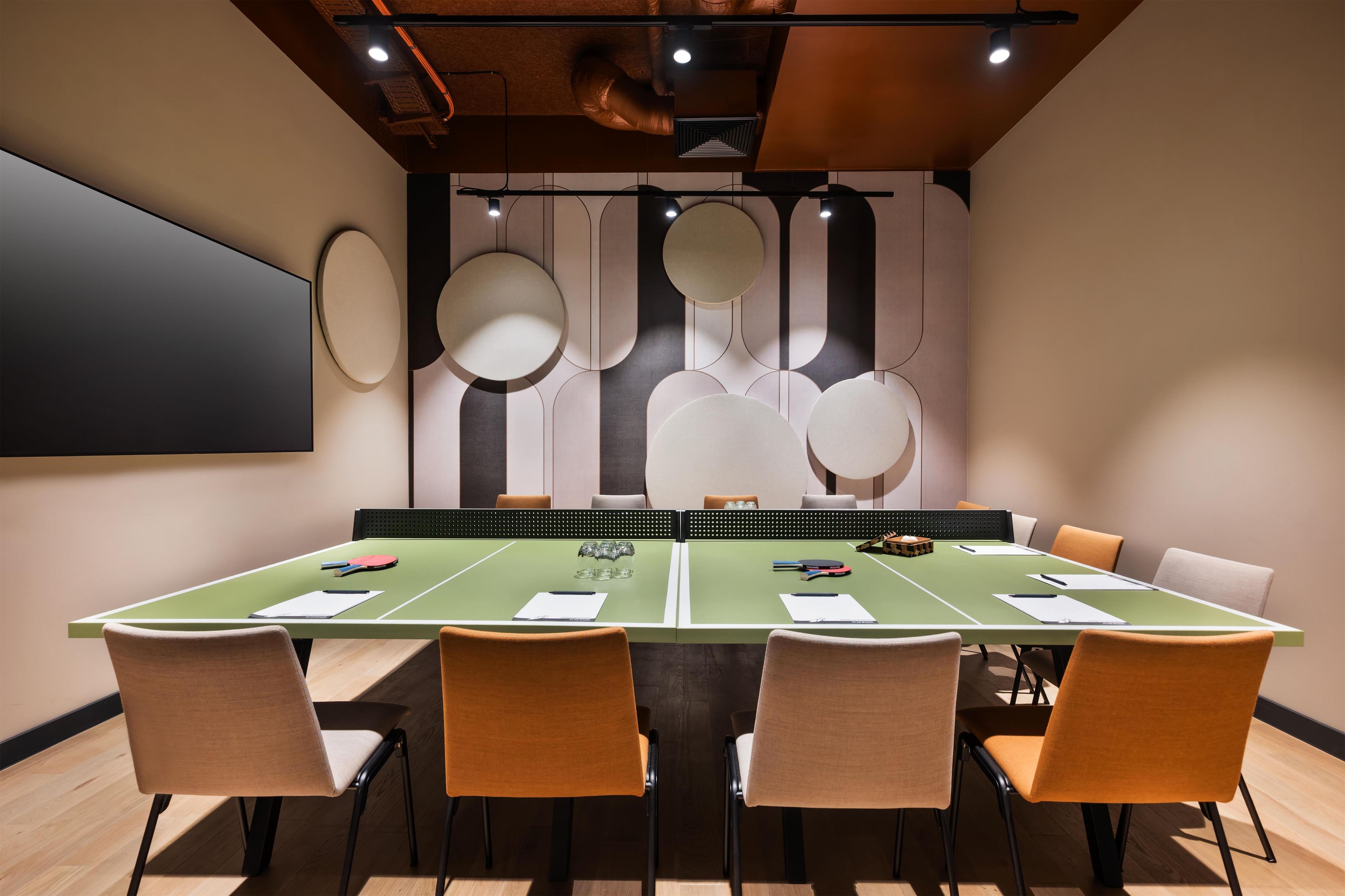 A conference room with a long table, chairs, and a large screen on the wall.
