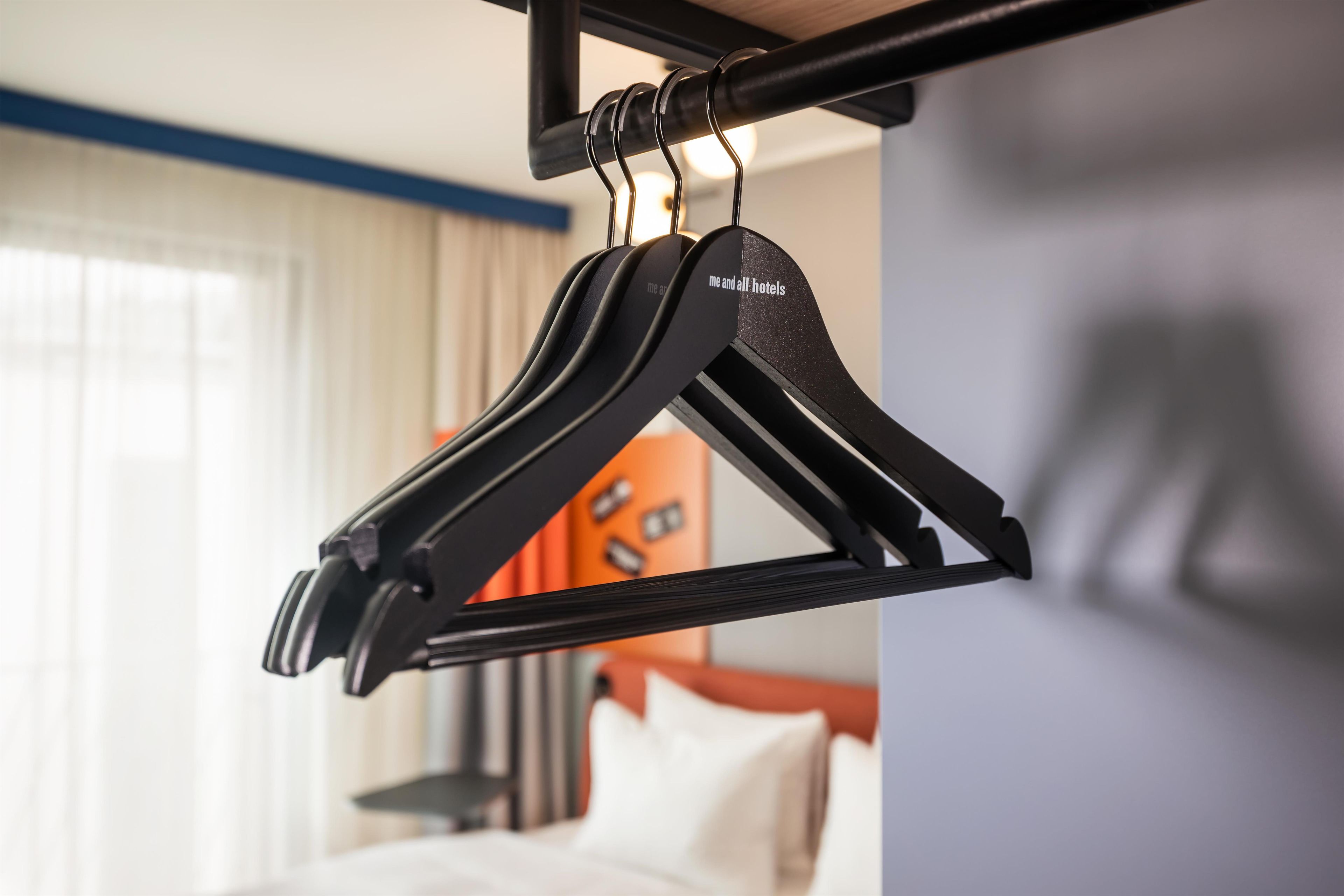 Um cabide preto com a frase 'me and all hotels' pendurada em uma barra de metal em um quarto de hotel.
