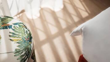 A room with a window casting shadows on a white pillow and a fabric with tropical leaf patterns.