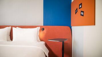 Ein Hotelzimmer mit einem Bett, einem kleinen Tisch und einer Wand mit einem blau-orangen Paneel.