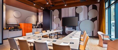 A modern conference room with a long table, chairs, and a television screen.