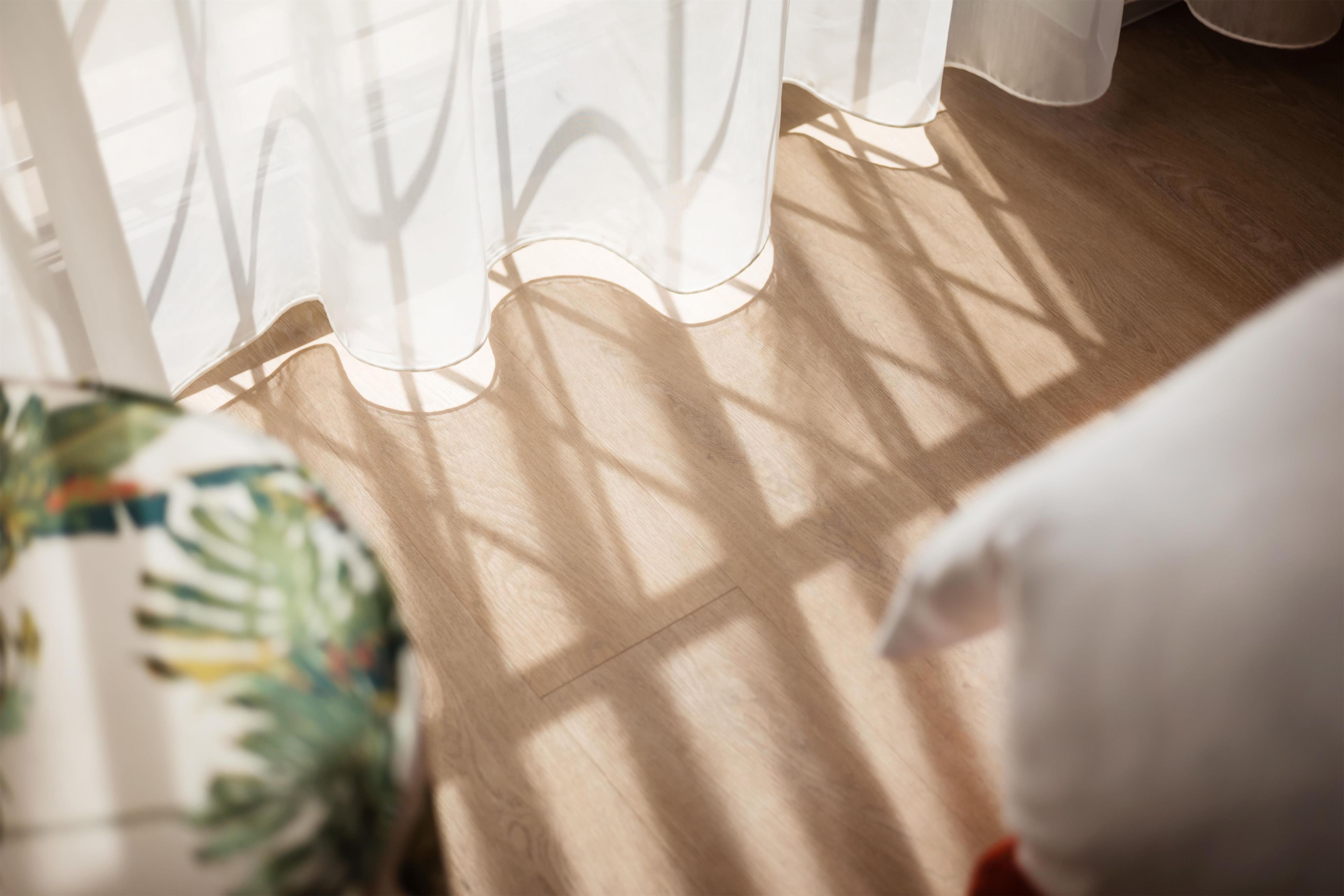 A wooden floor with a white curtain partially drawn back, allowing sunlight to cast shadows.