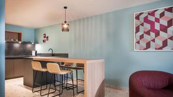 Cocina moderna con barra, dos taburetes de bar, un sillón rojo y una obra de arte geométrica en la pared.