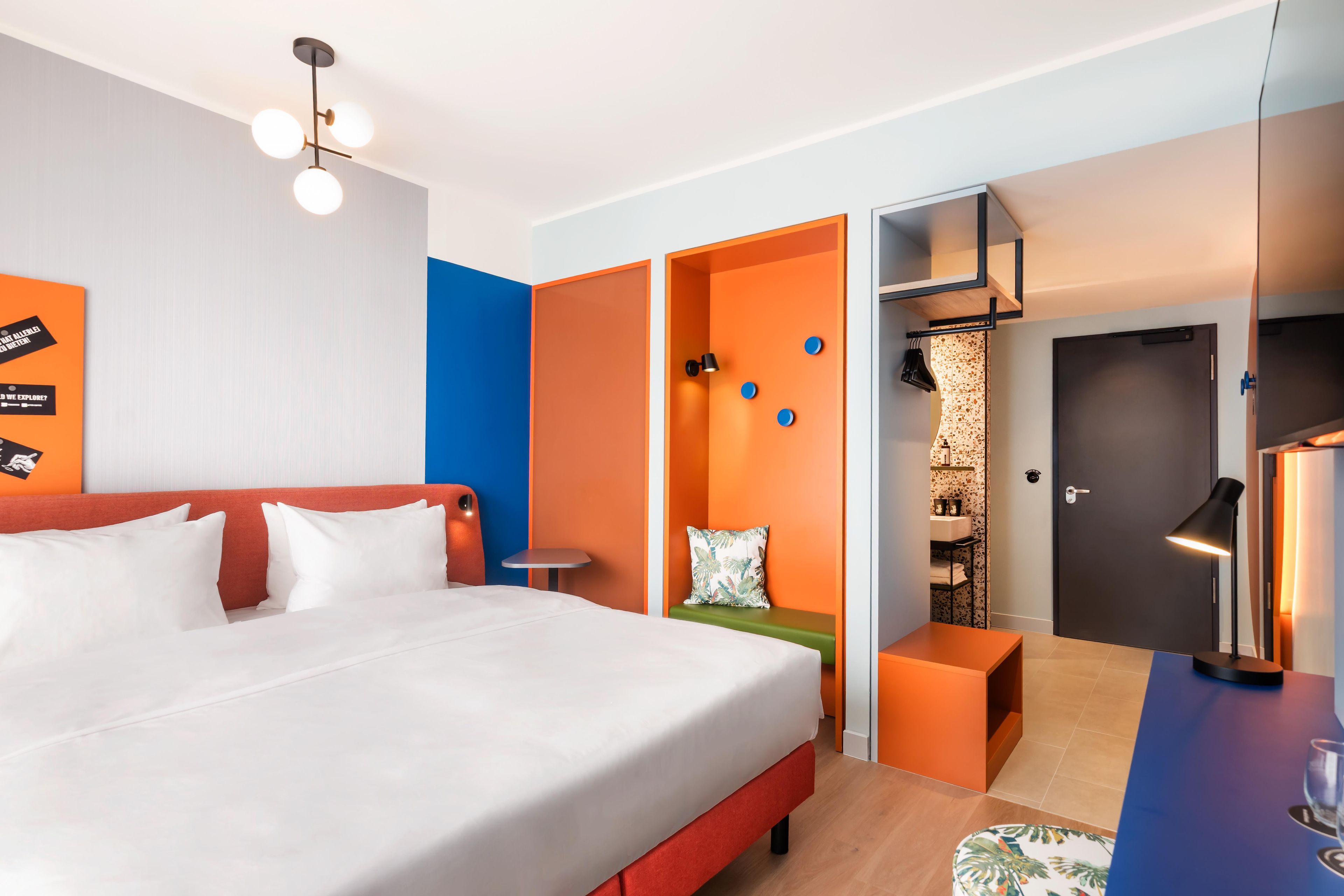 A modern hotel room with a large bed, a desk, and a walk-in closet.