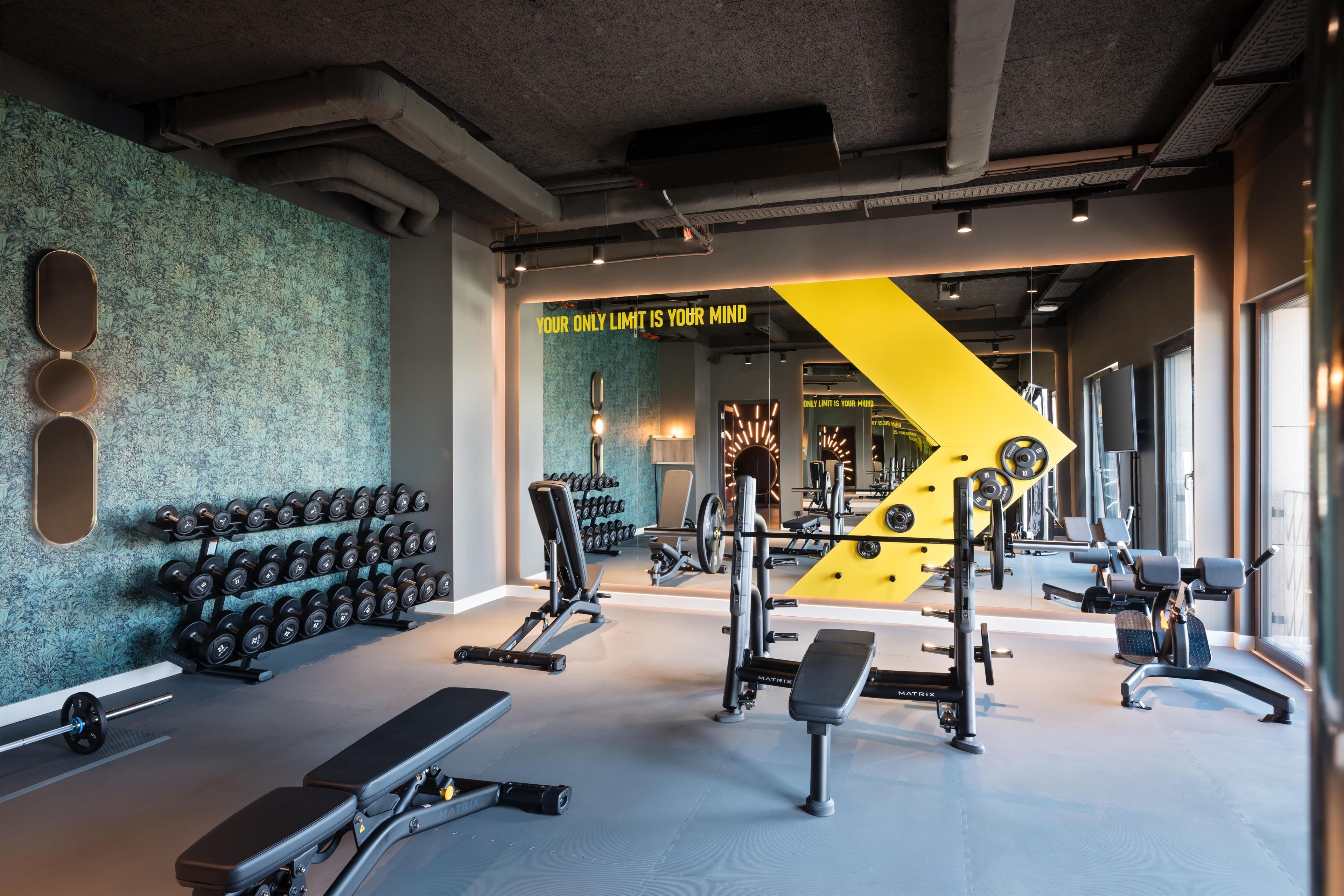 Academia com equipamentos de musculação, bancos e uma frase motivacional na parede.
