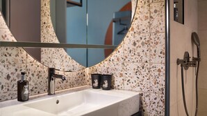 Un baño con un lavamanos blanco, un espejo redondo y una ducha.