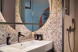 A bathroom with a white sink, a round mirror, and a shower. - Me and All Hotel Leipzig (LEIPZIG)