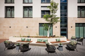 Pátio com área de estar externa e uma árvore central.