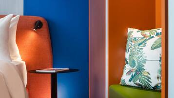 Una habitación con pared azul, una silla roja, una mesita redonda con una revista, y un sofá verde con un cojín estampado.