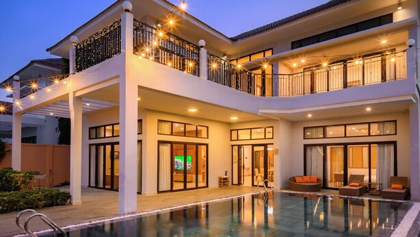 Un edificio de dos pisos con piscina, balcones iluminados con luces y una entrada visible con puertas de vidrio.