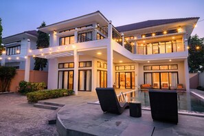 A two-story house with a swimming pool, outdoor seating, and string lights.