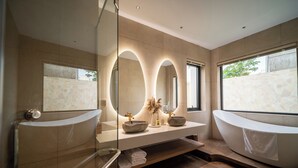 Un baño moderno con cabina de ducha de vidrio, una bañera independiente, un lavamanos con un espejo grande y una pared de piedra.