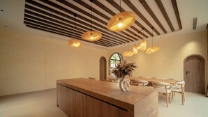 Una habitación amplia con un mostrador de recepción de madera, varias lámparas colgantes de mimbre y un gran ventanal de arco.