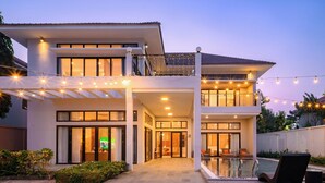 Una casa moderna de dos pisos con un porche cubierto, piscina y luces colgantes.
