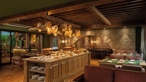 A restaurant with a stone wall, wooden ceiling beams, and a buffet setup. - The Evren, Vagator (GOA)