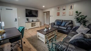 Uma sala de estar moderna com um sofá de couro, uma mesa de centro de madeira, uma escrivaninha com um globo e uma TV fixada na parede.