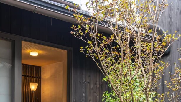 Een modern huis met een schuifdeur naar een gezellig interieur, een kleine tuin met stenen en begroeiing, en een houten gevel.