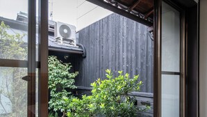 Een traditionele Japanse kamer met tatami vloeren, een shoji-scherm en uitzicht op een tuin met een bonsaiboom en een stenen lantaarn.