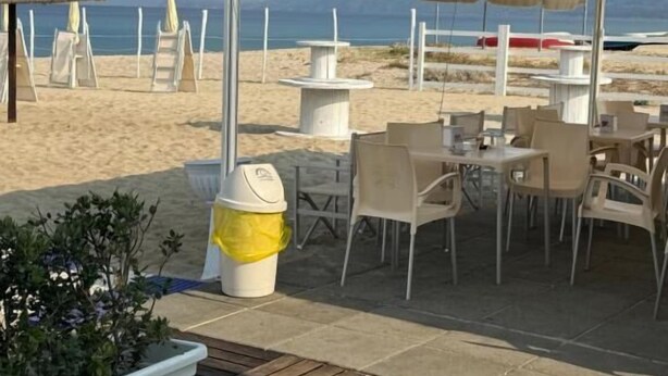 A beachside outdoor seating area with tables and chairs, a covered section, and a trash bin. - GLOBAL HOTEL (San Ferdinando)