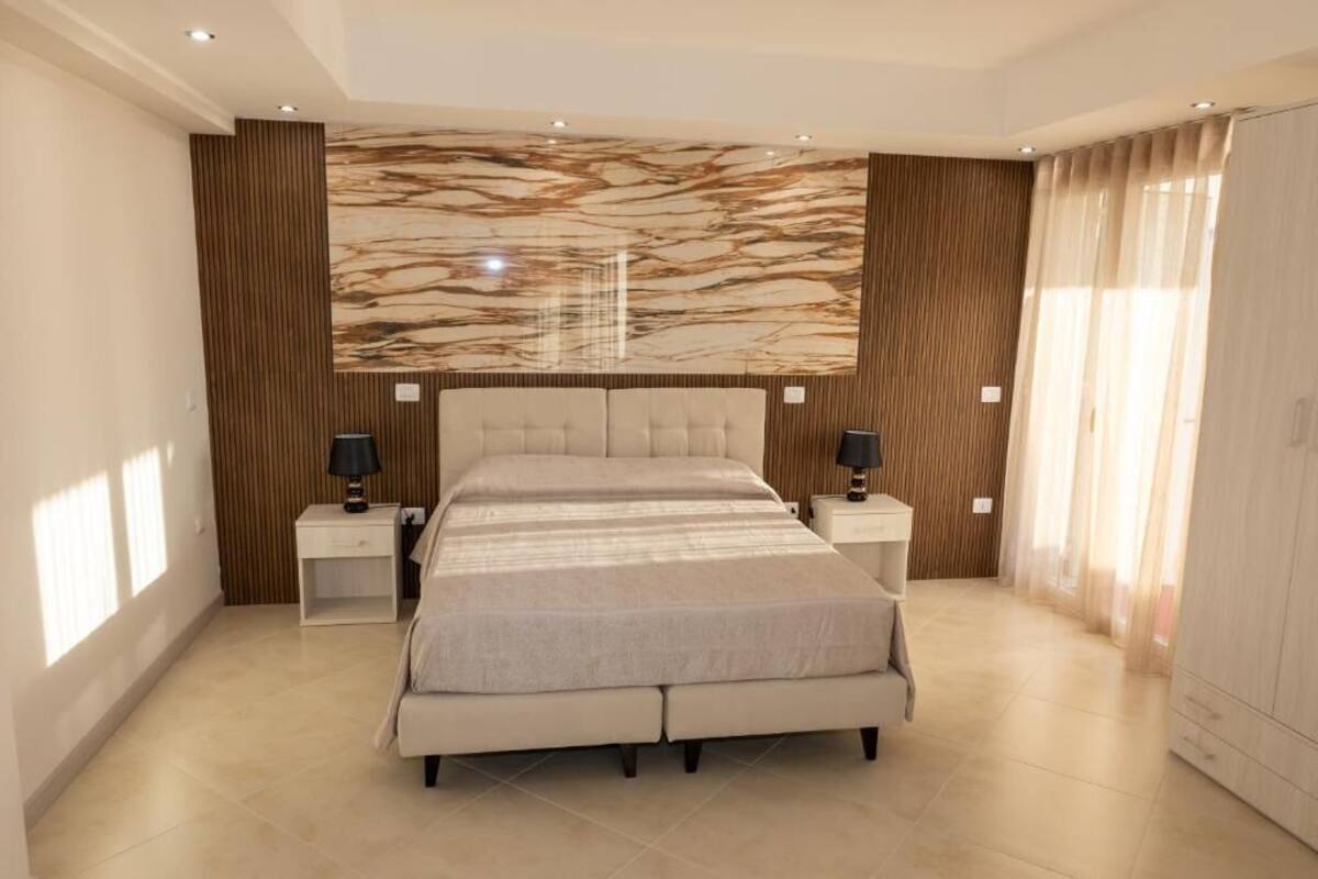A modern bedroom with a large bed, two bedside tables, and a marble-patterned wall.