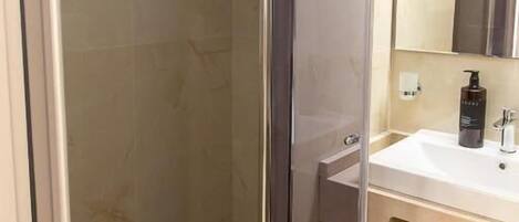 A modern bathroom with a glass shower enclosure, a white sink with a mirror, and a towel hanging on the wall.
