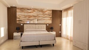 A modern bedroom with a large bed, two bedside tables with lamps, a marble-patterned wall, and a wardrobe. - GLOBAL HOTEL (San Ferdinando)