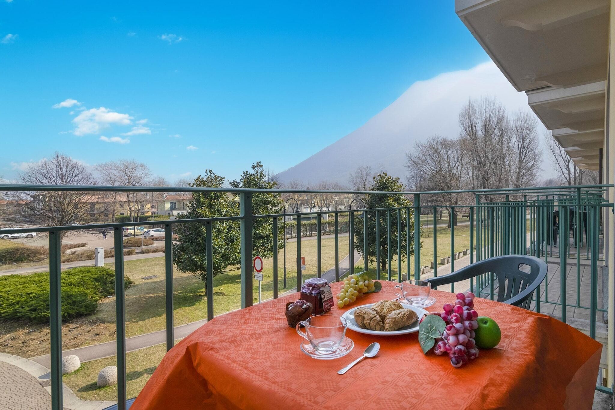 Un balcon avec une table préparée pour le petit-déjeuner, donnant sur un parc et une montagne.