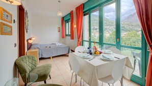 Una habitación con una mesa de comedor lista para dos personas, una cama y vistas a un paisaje montañoso a través de amplios ventanales.