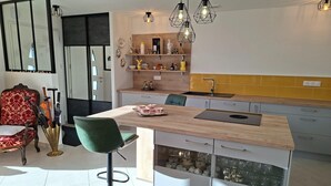 Une cuisine moderne dotée d’un îlot central, de luminaires suspendus et d’un coin repas avec un fauteuil à revêtement rouge.