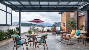 A covered outdoor patio with wicker furniture, potted plants, and a view of mountains. - Lijiang MAISON Hotel (Lijiang)