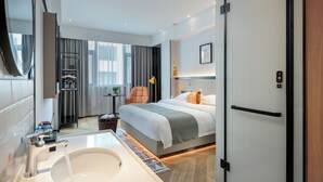 A modern hotel room with a large bed, a sitting area with a chair, a desk, and a large window. - Lijiang MAISON Hotel (Lijiang)