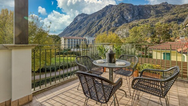 A balcony with wicker chairs and a table, overlooking a mountainous landscape. - Studio in Porlezza am Luganersee (Porlezza)