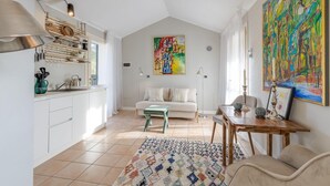 A bright kitchen with white cabinets, a dining area with a wooden table, and a colorful abstract painting on the wall. - Studio in Porlezza am Luganersee (Porlezza)