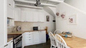 A compact kitchen with white cabinets, a microwave, and a stove. There is a dining table with chairs and a decorative basket. - Paros 3 bedrooms Maisonette for 6 persons by MPS (Molos)