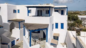 A white building with blue accents, featuring a covered outdoor seating area with a table and chairs. - Paros 3 bedrooms Maisonette for 6 persons by MPS (Molos)