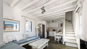 A modern living room with a sofa, a coffee table, and a staircase leading to a kitchen. - Paros 3 bedrooms Maisonette for 6 persons by MPS (Molos)