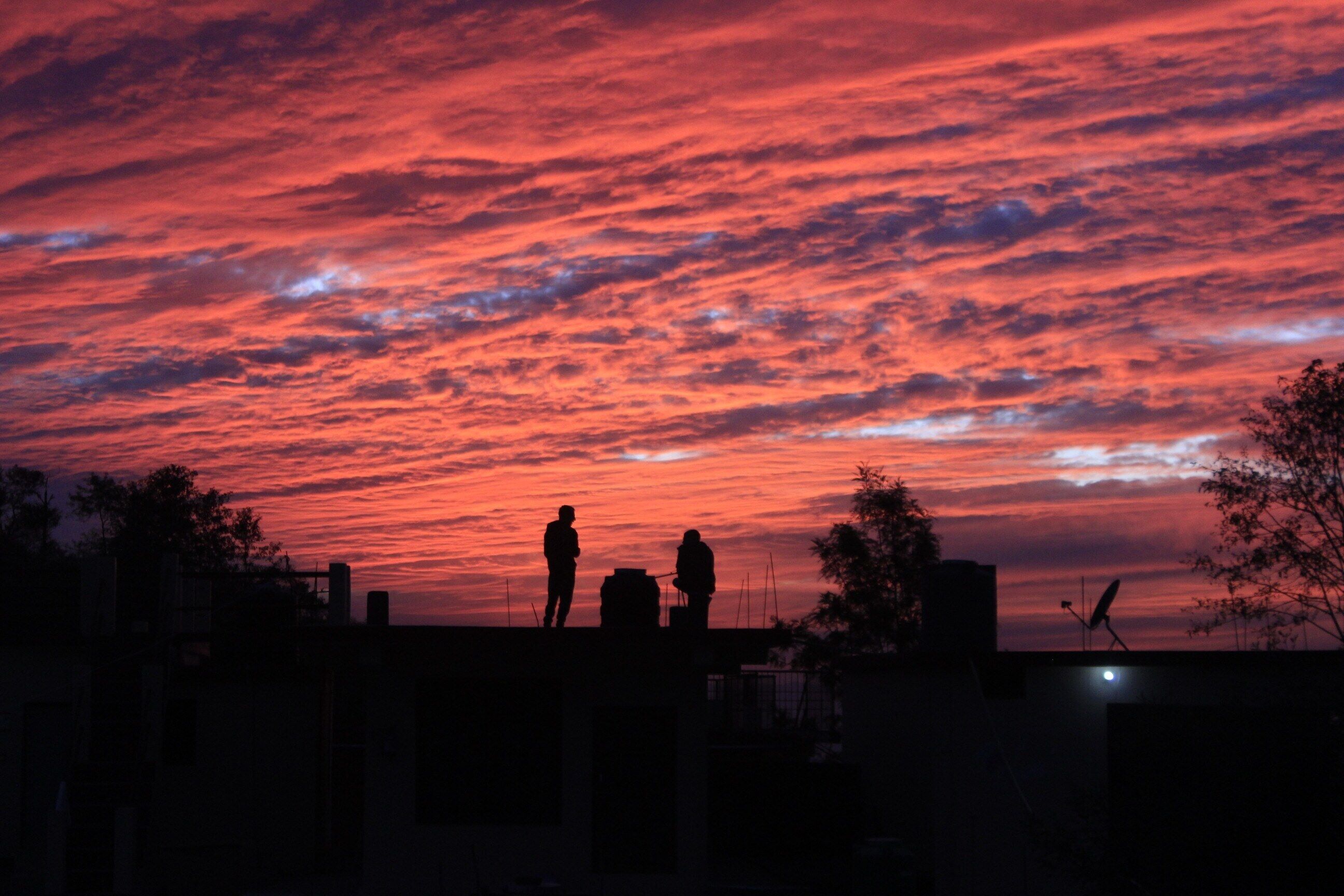 A sunset with two silhouetted figures on a rooftop.