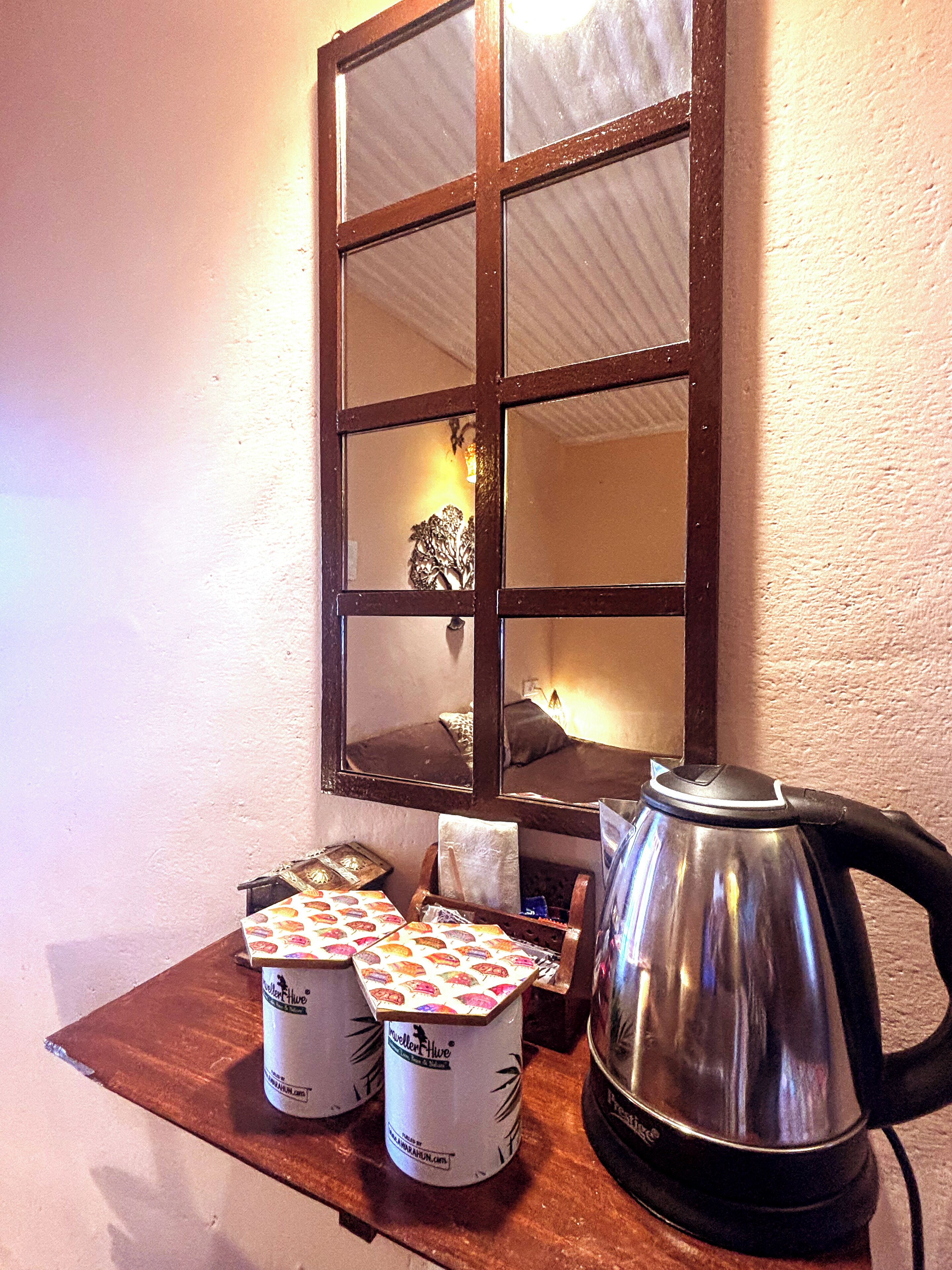 A kitchen area with a kettle, a wooden shelf with containers, and a window with a reflection.