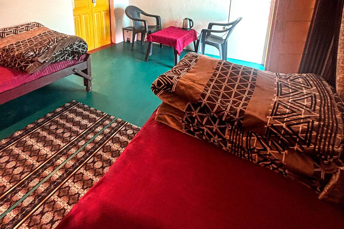 A room with two beds, a desk with a chair, a fan, and a door.