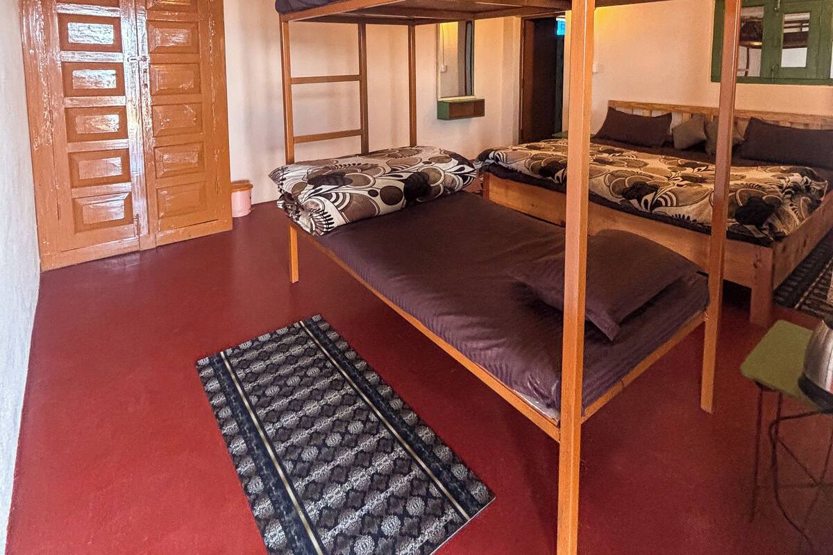 A bunk bed room with a red carpet, wooden door, and a patterned rug.