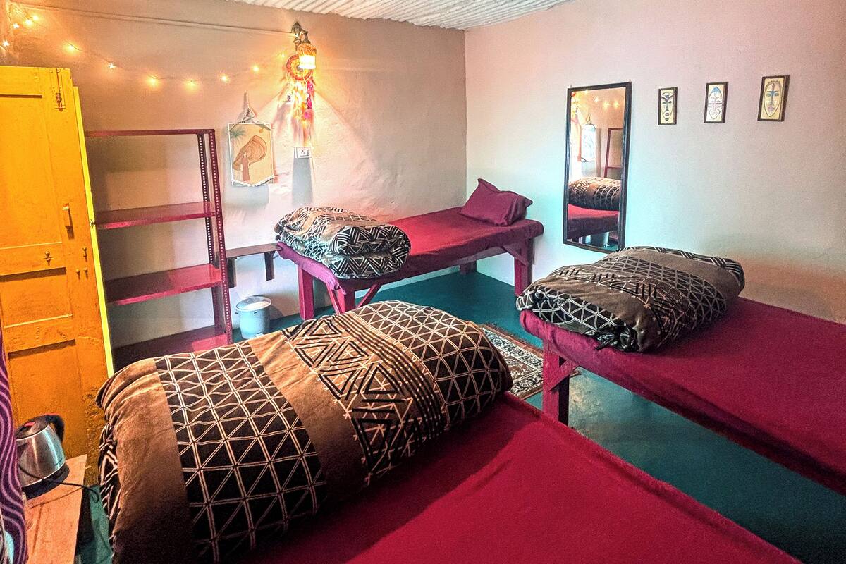 A room with two beds, a bench, a mirror, and string lights.